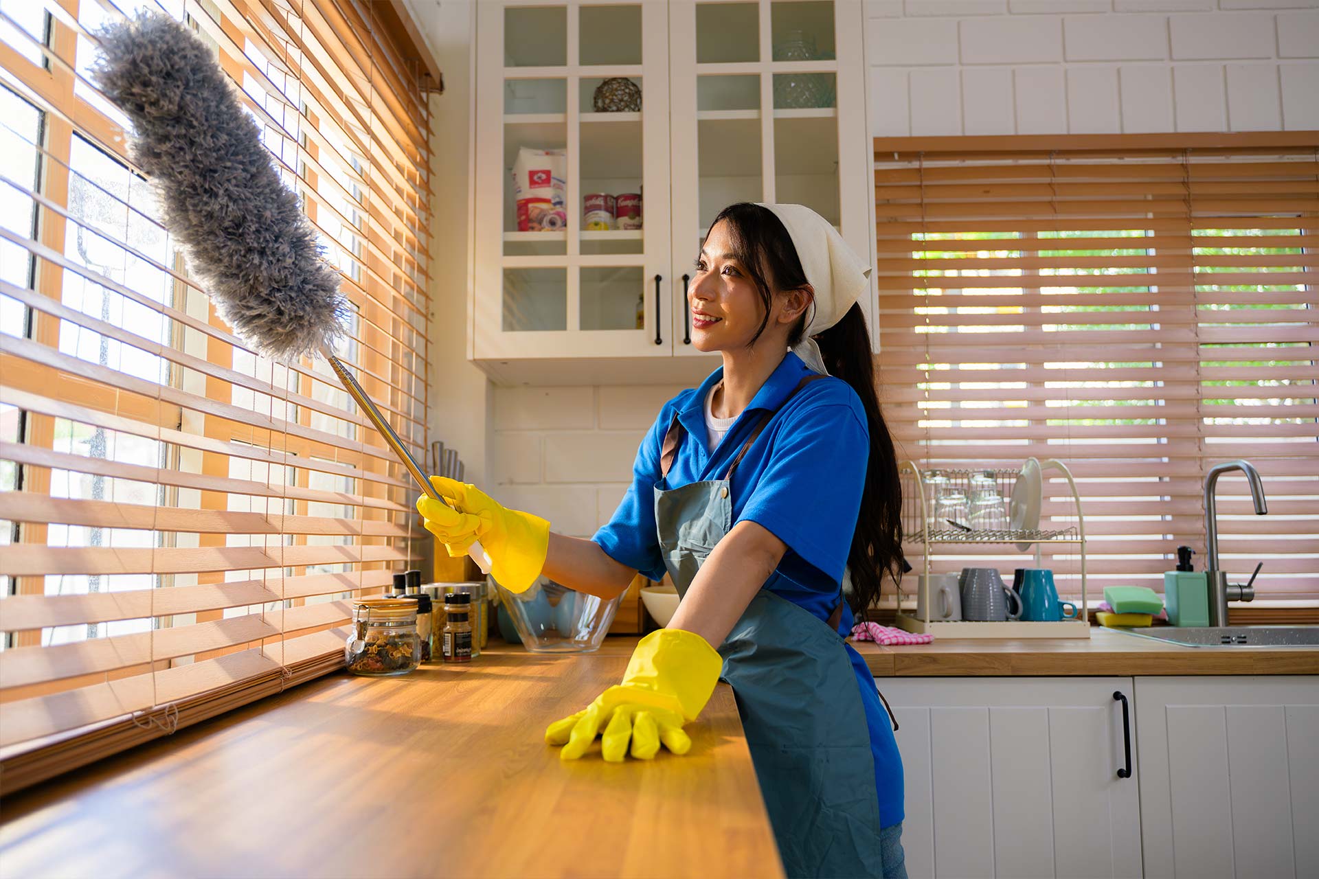 A complete uniformed smiling lady cleaning the window with a dust remover.